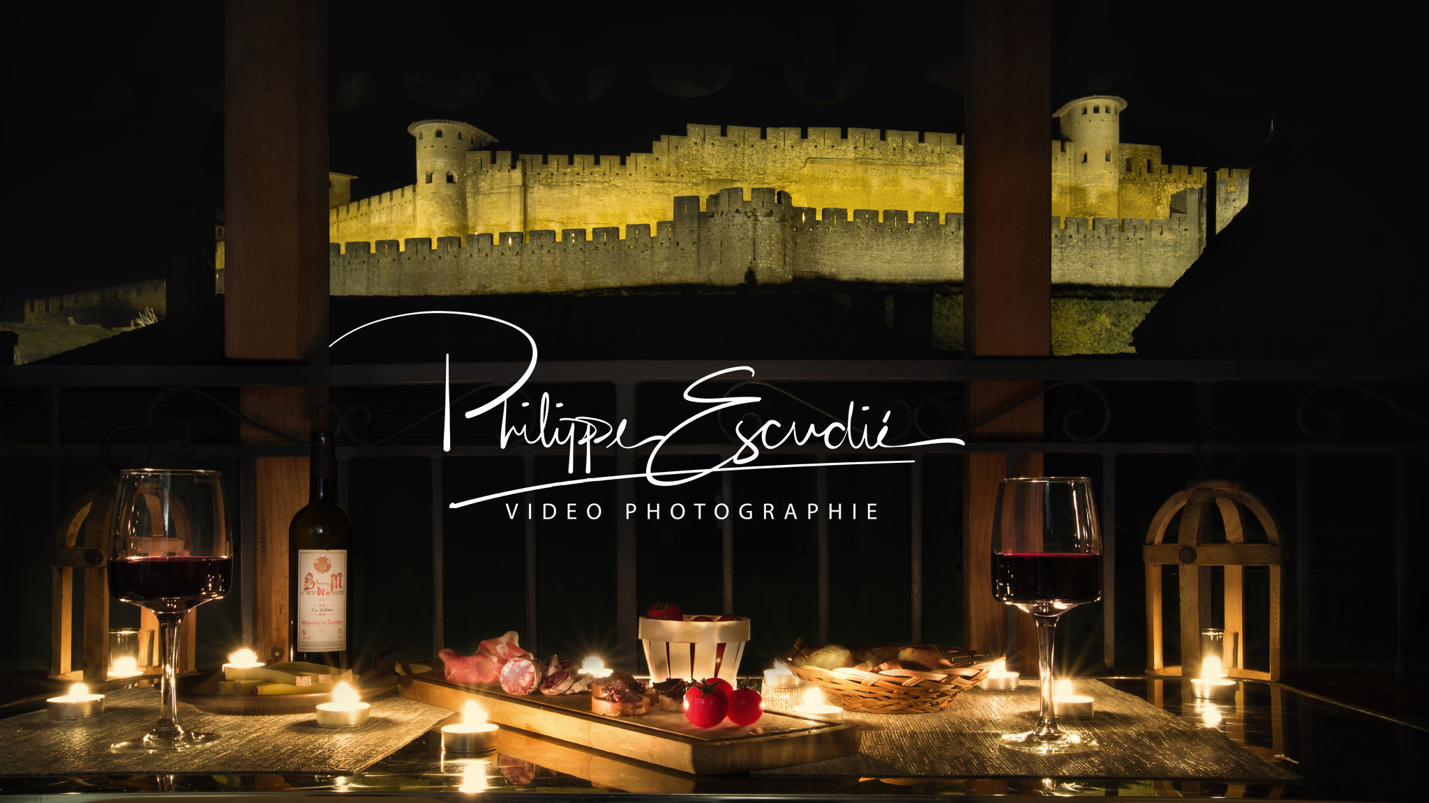 Ambiance apéritif de nuit sur une terrasse d'appartement, vin, charcuterie, bougie et la Cité de Carcassonne comme décor.