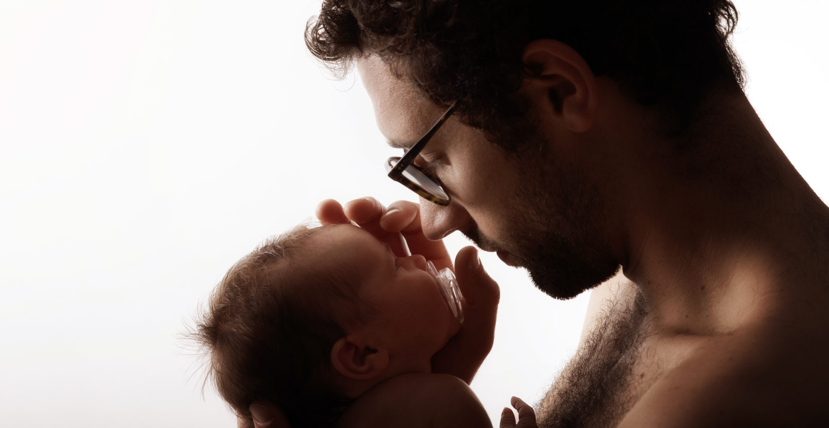 un homme avec des lunettes tient dans ses mains un bébé et lui caresse le front
