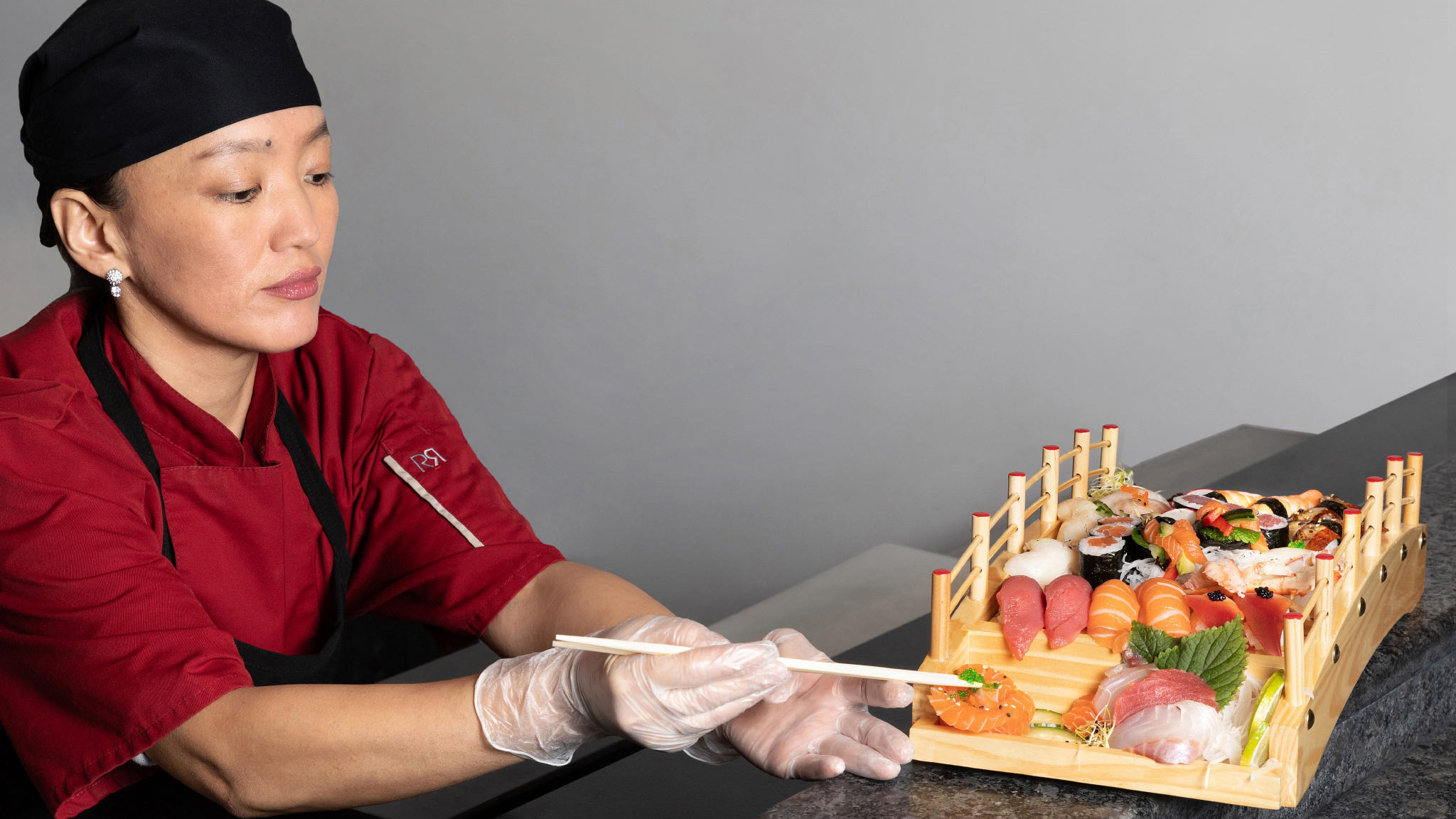 une chef cuisinière utilise des baguettes pour poser des oeufs de lompe sur un plat composé de sushis