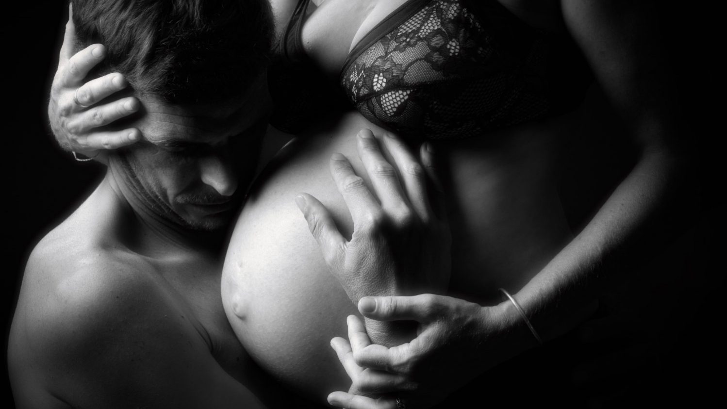 homme accroupi tenant le ventre d'une femme enceinte
