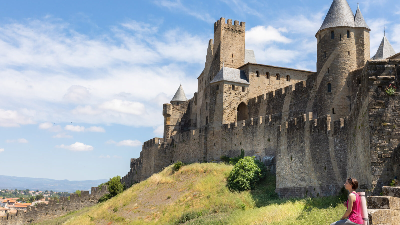 Une fille est assise devant les remparts d’une cité médiévale